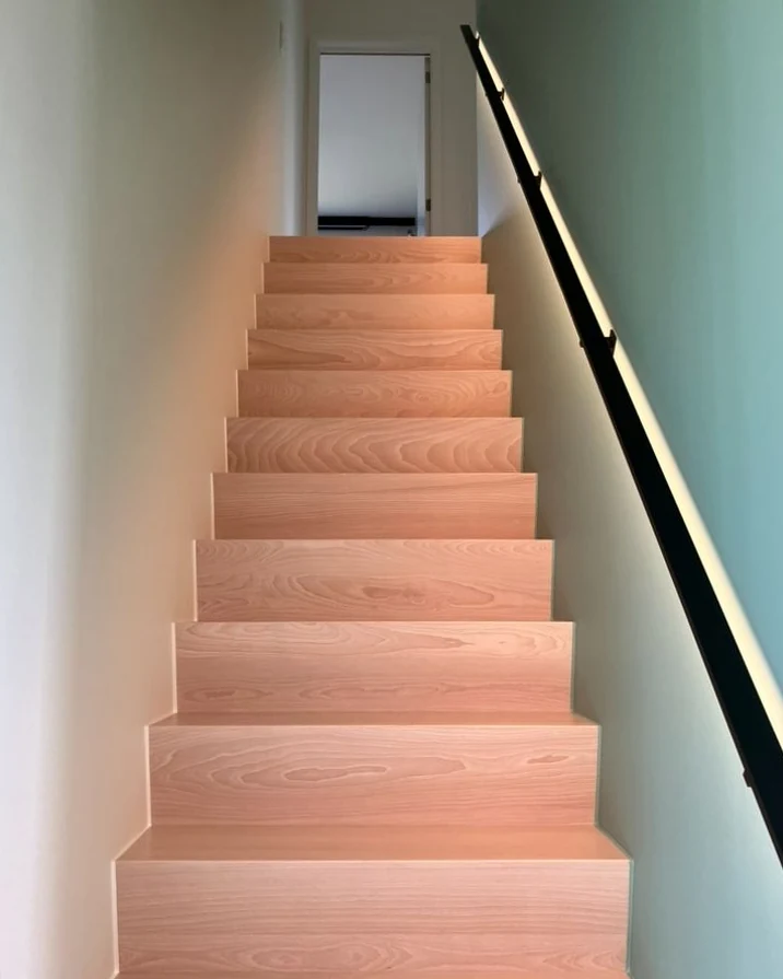 Trappenhal met een witte en een zachtgroene wand, beuken treden en een zwarte leuning